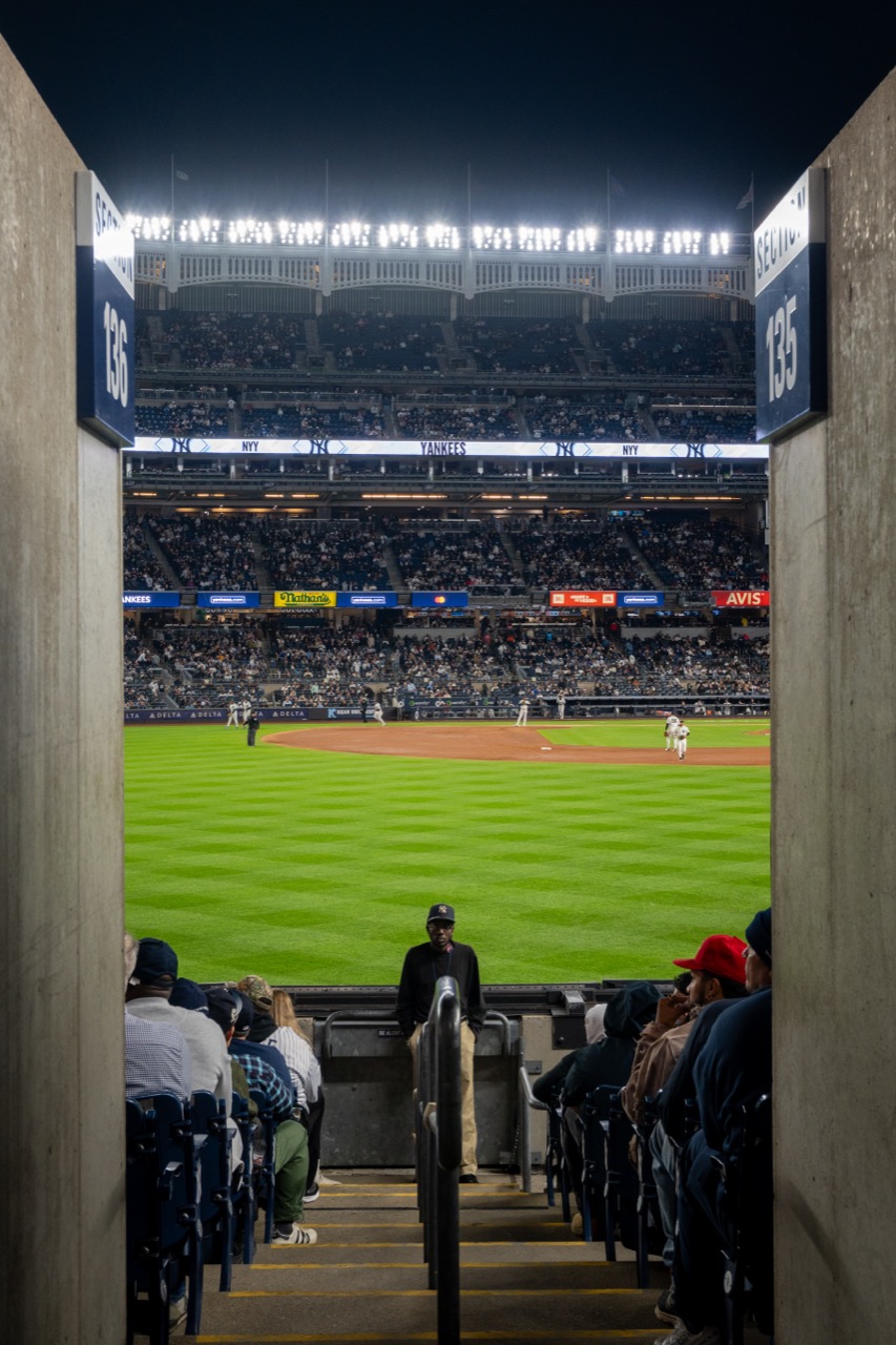 Night game at Yankee Stadium viewed through a concourse tunnel onto the floodlit field